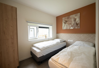 Dormitorio luminoso con dos camas individuales, ventana y cuadro natural en Holiday Park Zeebad 14, Países Bajos.