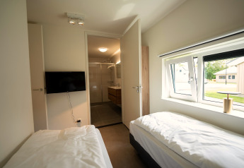 Moderne soveværelse med to enkeltsenge, TV på væggen og udsigt til badeværelse i Holiday Park Zeebad.