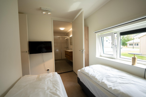 Habitación moderna con dos camas individuales, TV y baño privado en Holiday Park Zeebad, Países Bajos.