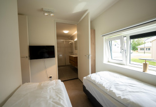 Camera moderna con due letti singoli, TV a parete e bagno privato al Holiday Park Zeebad nei Paesi Bassi.