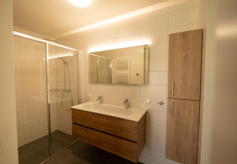 Baño moderno con ducha de vidrio, doble lavabo, espejo grande y armarios de madera en Zeebad 14, Países Bajos.