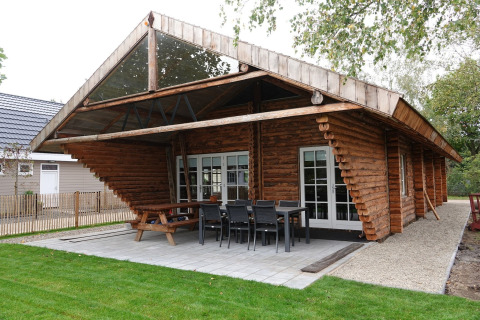 Cabaña de madera Park de Kievit 11 con terraza cubierta, conjunto de comedor exterior y césped.