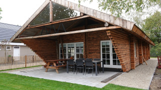 Holzchalet Park de Kievit 11 mit überdachter Terrasse, Sitzbereich und grüner Rasenfläche davor.
