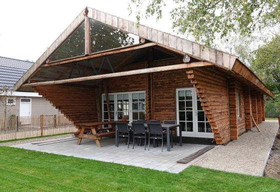 Træchalet Park de Kievit 11 med stor overdækket terrasse, havebord og stole på flisebelagt område.