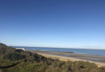 View from Holiday Park Zeebad 14 lodge in the Netherlands, showing beach, sea, blue sky and coastal bushes.