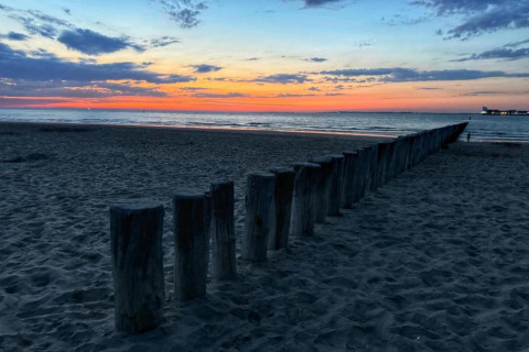 Sonnenuntergang am Meer mit Holzpfählen im Sand, Ausblick von einer Lodge-Strand, bunte Abendhimmel.