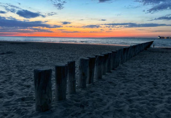 Atardecer junto al mar con postes de madera en la arena, vista desde una playa de lodge, cielo colorido.