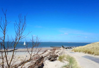 Udsigt fra en lodge til sandklitter, strand, hav og sejlbåd under en klar blå himmel.
