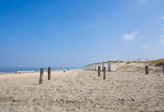 Spiaggia sabbiosa con cabine bianche, pali di legno e poche persone vicino a un lodge sul mare.