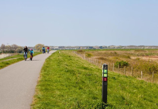 Ciclisti percorrono una pista ciclabile tra i campi e vicino a un cartello, sotto un cielo limpido presso un lodge.