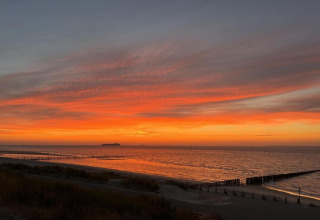 Stunning sunset view from a lodge overlooking the sea, vibrant sky, and a ship on the horizon.