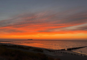 Stunning sunset view from a lodge overlooking the sea, vibrant sky, and a ship on the horizon.