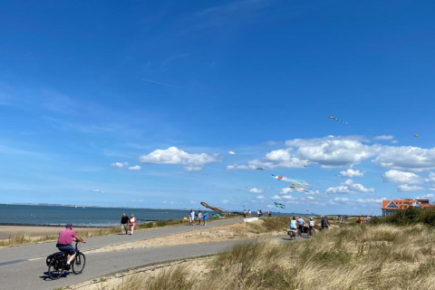 Folk cykler og går langs kysten ved Holiday Park Zeebad 14 i Holland, blå himmel og drager i luften.
