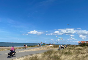 People cycling and walking by the coast near Holiday Park Zeebad 14 in the Netherlands, kites in the sky.