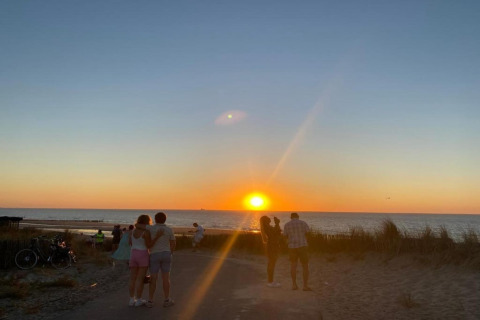 Personer nyder en smuk solnedgang ved havet, omgivet af strand og klitter ved et sommerhus.