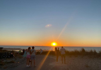 People watch a beautiful sunset by the sea, surrounded by sand dunes near a beachside lodge.