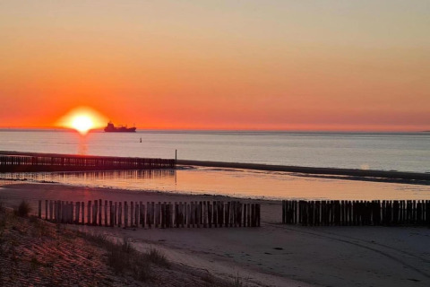 Coucher de soleil sur la mer depuis Holiday Park Zeebad 14 aux Pays-Bas, avec un navire à l’horizon.