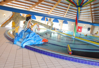 Piscina cubierta en un lodge con figuras infantiles, tobogán y una colorida columna central decorativa.