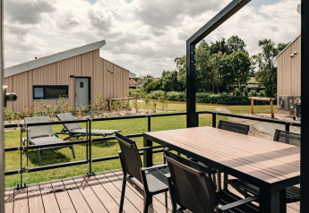 Patio with dining table and loungers at Holiday Park Zeebad 11, Netherlands, modern lodge with green lawn.