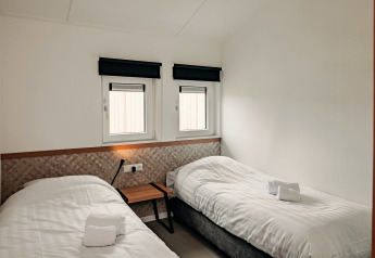 Bright, minimal lodge room with two single beds, white bedding, two windows, and a modern design.