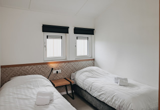 Bright, minimal lodge room with two single beds, white bedding, two windows, and a modern design.