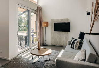 Moderne opholdsstue i Holiday Park Zeebad 11, Nederlandene, med stor sofa, tv og udsigt til terrasse.