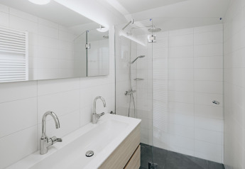 Baño moderno con doble lavabo, ducha amplia y gran espejo en Holiday Park Zeebad 11 en los Países Bajos.