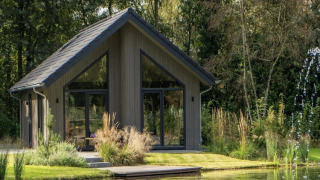 Lodge moderno en Holiday Park Latour 4, junto a un estanque, rodeado de vegetación y grandes ventanales.