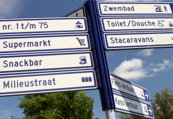 Vejskilte ved en lodge, der viser retninger til supermarked, snackbar, toiletter og swimmingpool.