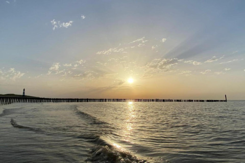 Zonsondergang aan zee bij Holiday Park Zeebad 11 met zachte golven en een vuurtoren in de verte, Nederland.