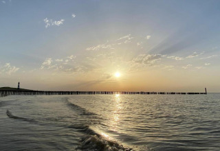 Zonsondergang aan zee bij Holiday Park Zeebad 11 met zachte golven en een vuurtoren in de verte, Nederland.