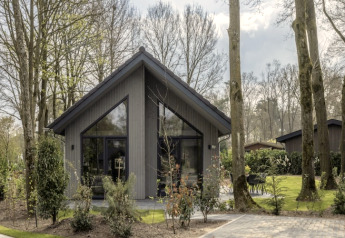 Feriehytte i Holiday Park Latour 6, omgivet af træer og grønt, moderne design med stor glasfacade.