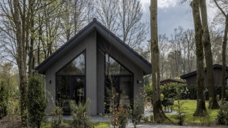 Feriehytte i Holiday Park Latour 6, omgivet af træer og grønt, moderne design med stor glasfacade.