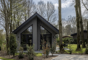 Feriehytte i Holiday Park Latour 6, omgivet af træer og grønt, moderne design med stor glasfacade.