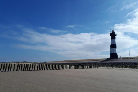 Et billede af en sort og hvid fyrtårn på en strand med blå himmel og skyer i baggrunden.
