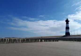 Foto de un faro blanco y negro en la playa de arena bajo un cielo azul con algunas nubes dispersas.
