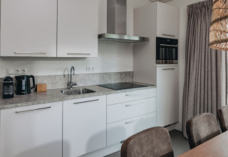 Modern kitchen at Holiday Park Zeebad 12 in the Netherlands with white cabinets, appliances, and dining table.