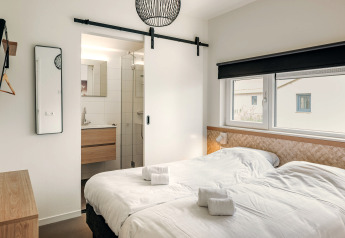 Moderne soveværelse med to enkeltmandsenge, badeværelse en suite og store vinduer i Holiday Park Zeebad.