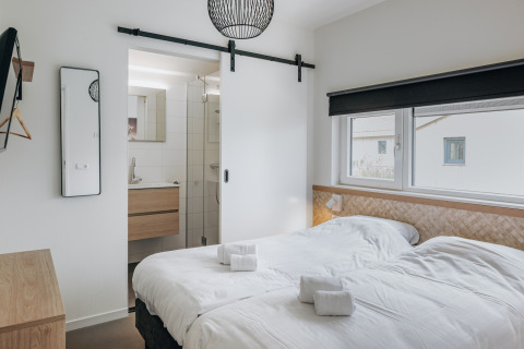 Habitación moderna con dos camas individuales, baño privado y grandes ventanas en Holiday Park Zeebad 12.