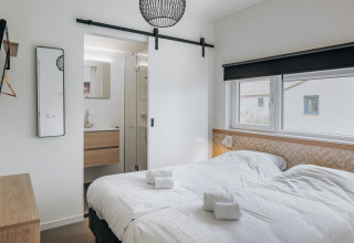 Modern bedroom with twin beds, en-suite bathroom and large windows at Holiday Park Zeebad 12 in the Netherlands.