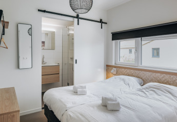 Modern bedroom with twin beds, en-suite bathroom and large windows at Holiday Park Zeebad 12 in the Netherlands.
