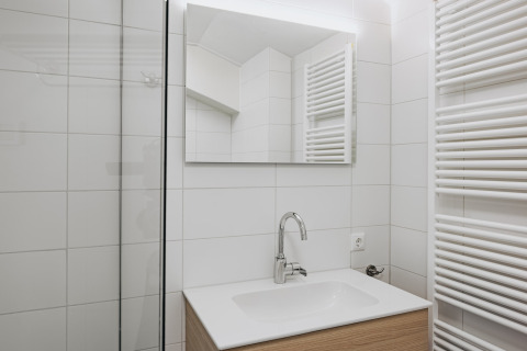 Baño moderno con lavabo blanco, espejo, grifo cromado y radiador en Holiday Park Zeebad 12, Países Bajos.