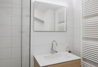 Bagno moderno con lavabo bianco, specchio, rubinetto cromato e radiatore a Holiday Park Zeebad 12, Paesi Bassi.