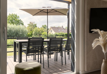 Udsigt fra indendørs til terrasse med spisebord, stole og parasol i Holiday Park Zeebad 12, Holland.