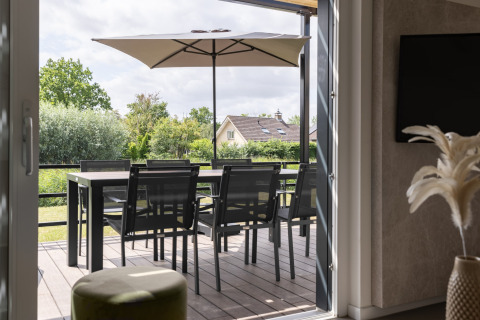 Udsigt fra indendørs til terrasse med spisebord, stole og parasol i Holiday Park Zeebad 12, Holland.
