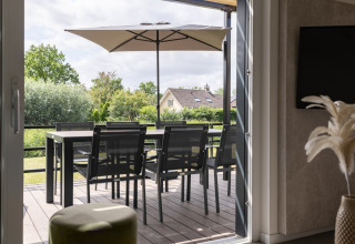 Udsigt fra indendørs til terrasse med spisebord, stole og parasol i Holiday Park Zeebad 12, Holland.