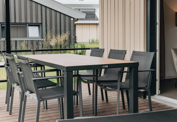 Outdoor dining area on a wooden terrace at Holiday Park Zeebad 12 lodge, Netherlands, with modern chairs.