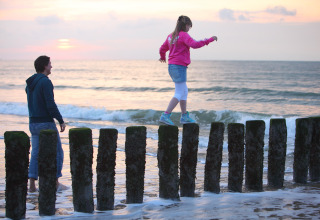 Una ragazza cammina in equilibrio su pali di legno al tramonto a Holiday Park Zeebad 12, nei Paesi Bassi.