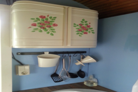 Küchenbereich im Mobilheim Pipowagen de Weideblick, Schrank mit Blumenmotiv und Utensilien an Haken.