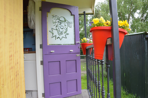 Lilla dør med klovnemotiv i mobilhjem Pipowagen 'de Weideblick', Holland, blomster i røde potter.